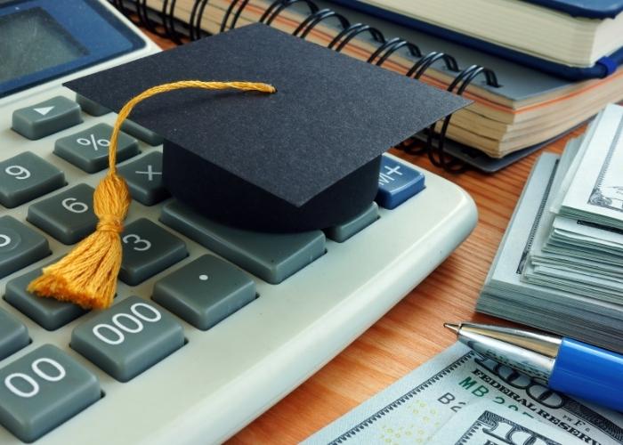 graduation cap on calculator with pen and dollar bills